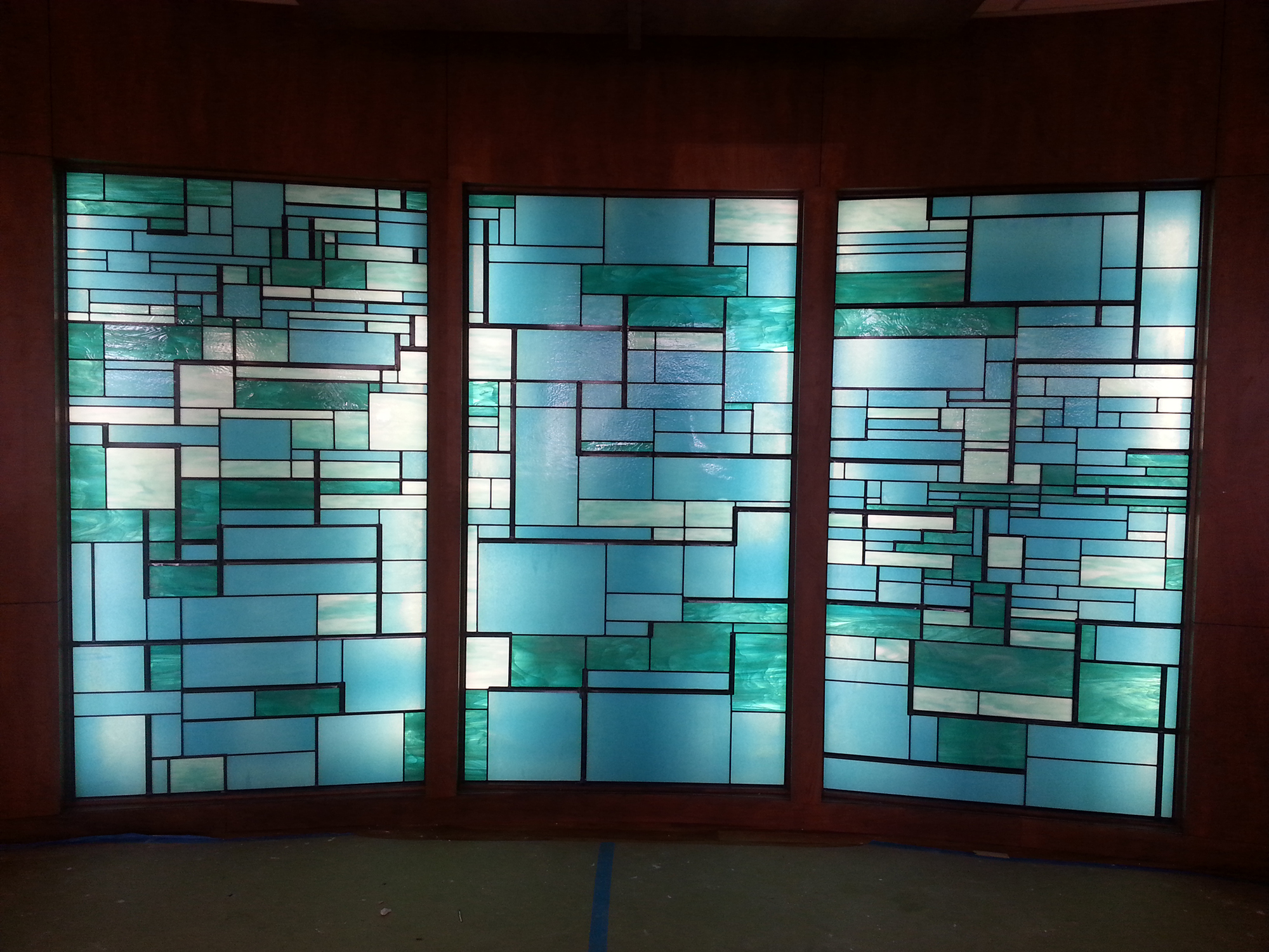 3 rectangular stained glass windows with modern, linear design. Hues of blue, green and white