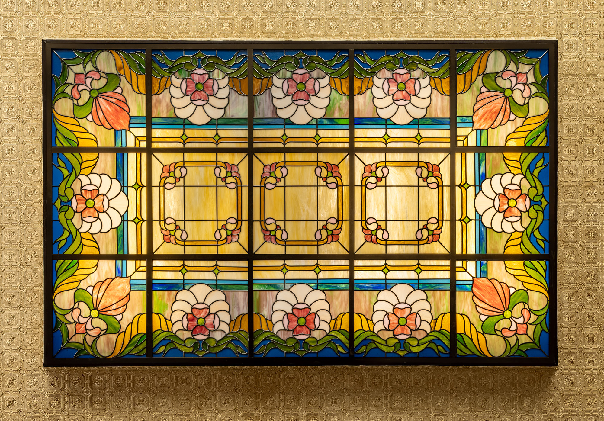 areal view of lit dropped ceiling with stained glass in the art nouveu style. swirly amber glass with pink flowers, blue border