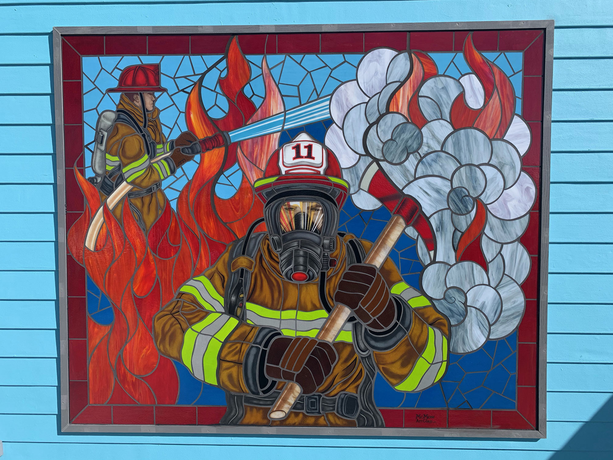 Traditional style stained glass window of a fire fighter with red, yellow, and blue glass.