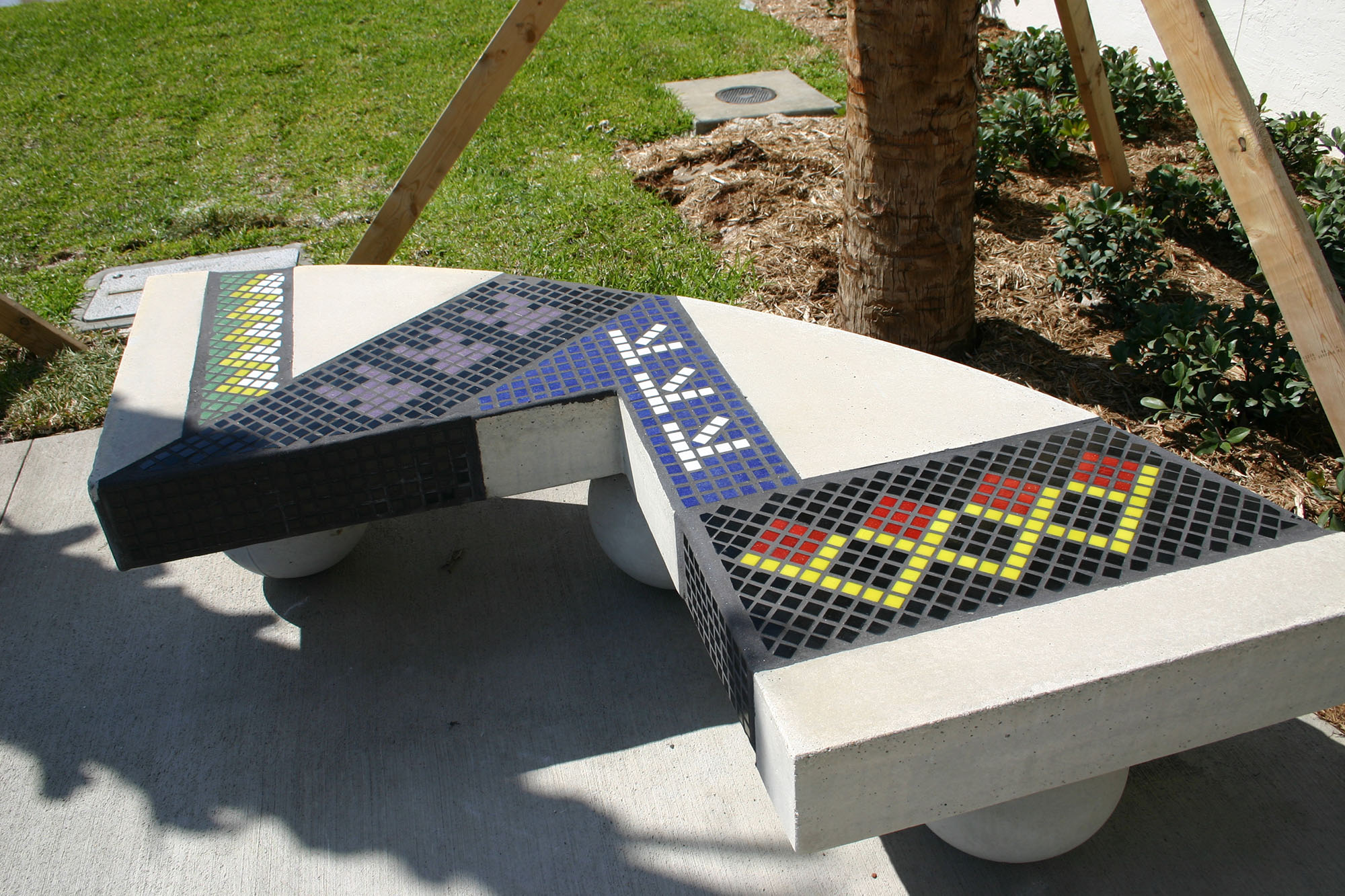 Public art mosaic bench with blue, black, green, yellow, and red colored glass in a traditional style.