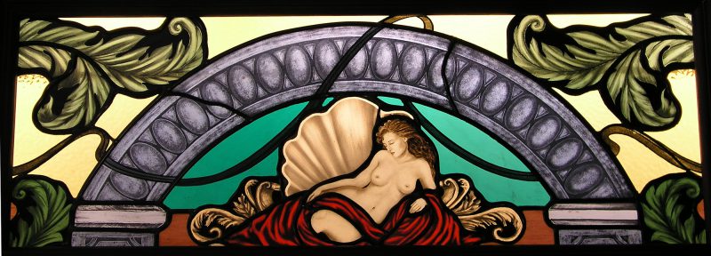 stained glass window with woman in the nude laying on shell. Purple arch over her with green leaves