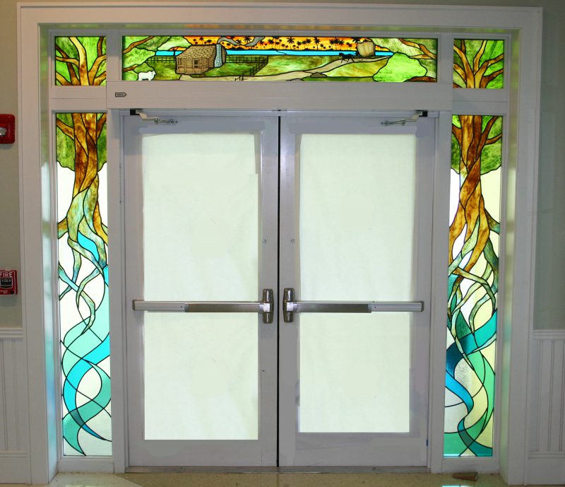 Entryway of trees and its roots with brown, green, and blue colored glass in a traditional style.