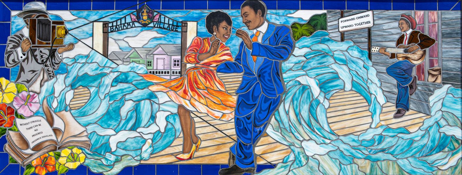 Mosaic of a man and woman dancing with blue waves around them in blue and orange colored glass, in a traditional style.