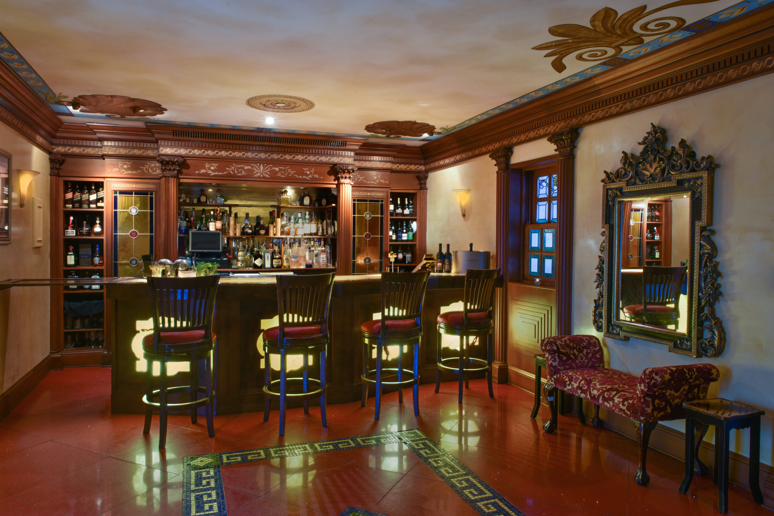 traditional bar area with 4 bar stools, wooden built ins and stained glass windows to the right