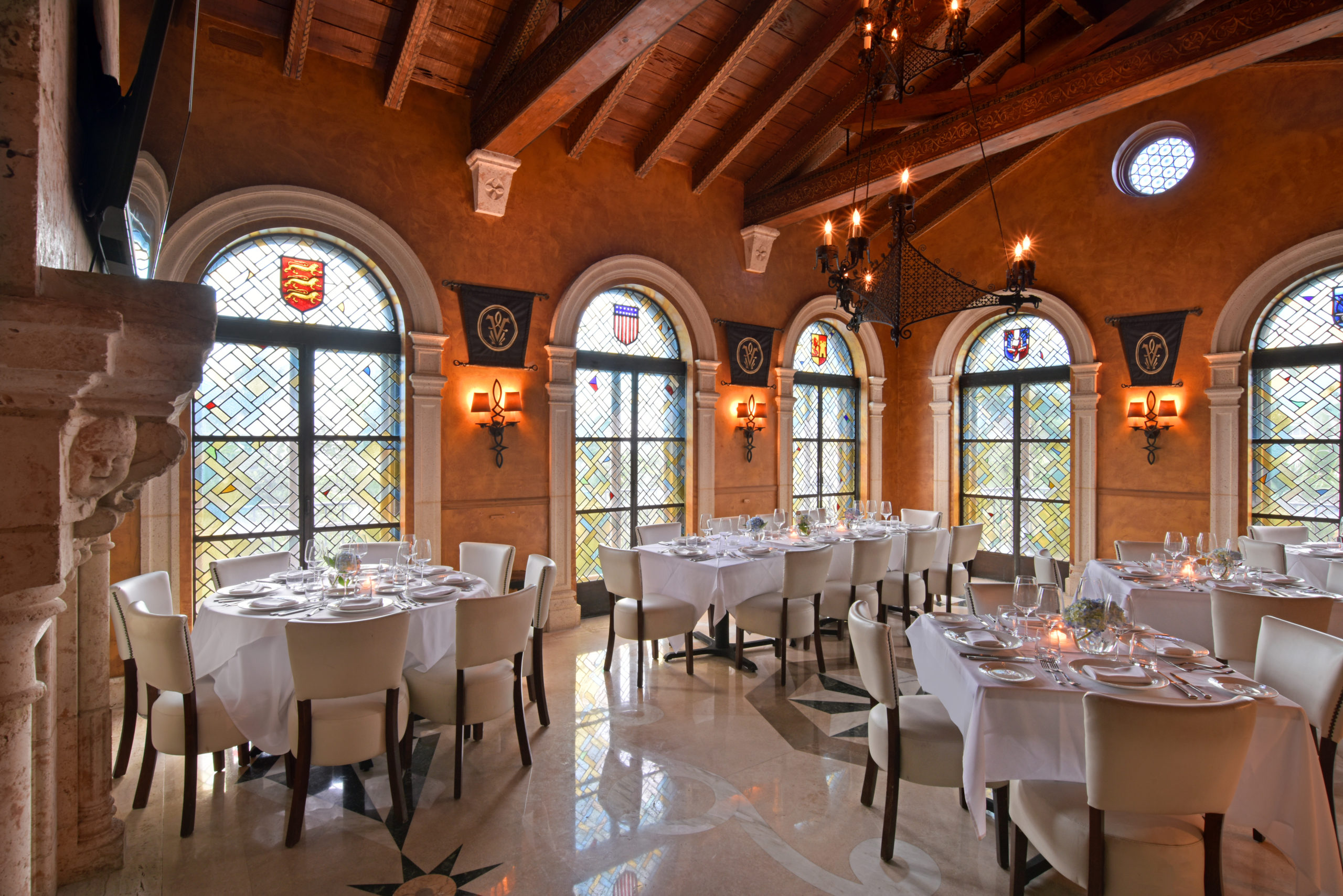dining space with white table cloths, white chairs and arched windows with traditional style stained glass